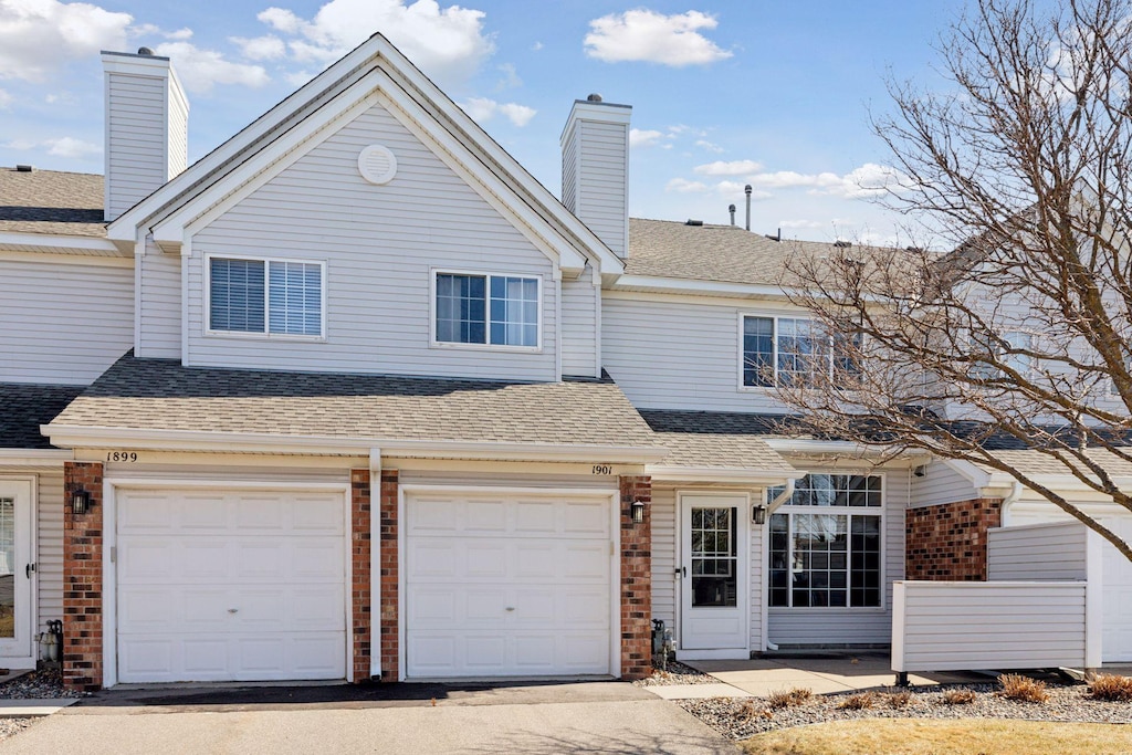townhome / multi-family property featuring brick siding, aphalt driveway, a garage, and roof with shingles