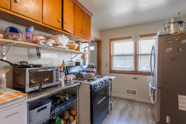 kitchen featuring light wood finished floors, a toaster, visible vents, freestanding refrigerator, and range with gas stovetop