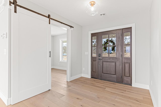 entryway with light wood-type flooring, baseboards, and a barn door