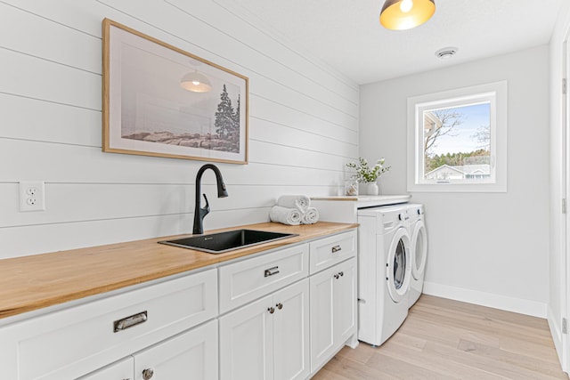 clothes washing area with light wood-style flooring, visible vents, a sink, baseboards, and washing machine and dryer