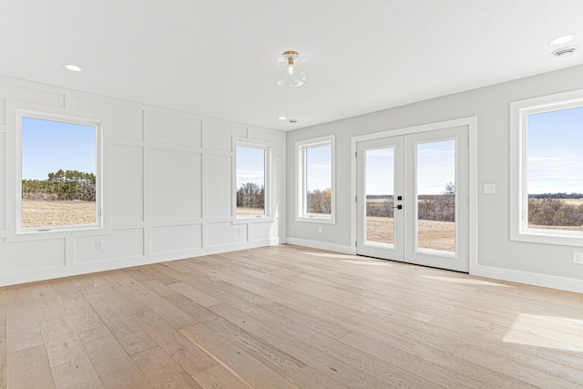 spare room featuring a decorative wall, french doors, light wood-style flooring, and baseboards