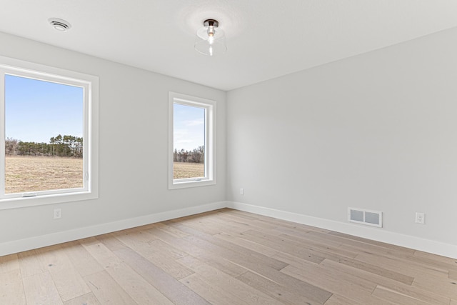 empty room with light wood-style floors, baseboards, and visible vents