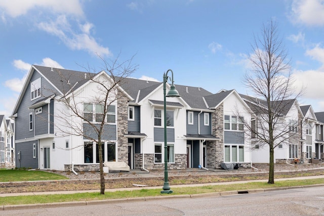 townhome / multi-family property with a residential view, board and batten siding, roof with shingles, and stone siding