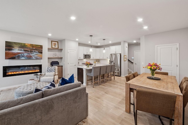 living area featuring stairs, recessed lighting, a glass covered fireplace, and light wood-style floors