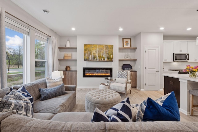 living area with recessed lighting, a glass covered fireplace, and light wood-style flooring