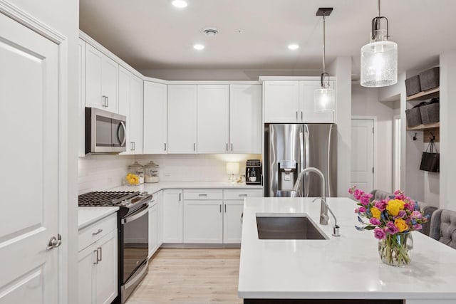 kitchen featuring pendant lighting, a center island with sink, light countertops, a sink, and stainless steel appliances