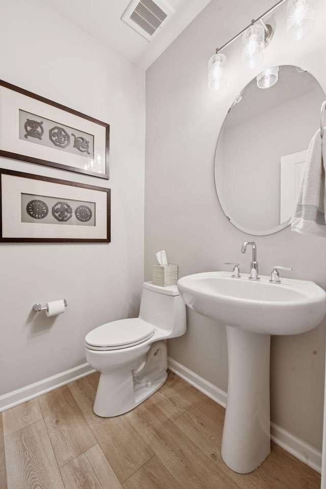 bathroom with baseboards, toilet, wood finished floors, and visible vents