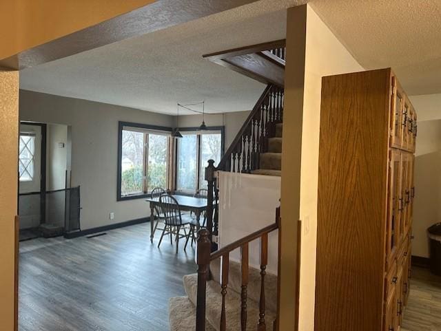 stairway with a textured ceiling, wood finished floors, and baseboards