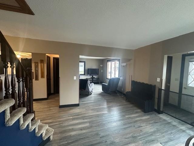 unfurnished living room with a textured ceiling, wood finished floors, baseboards, and stairs