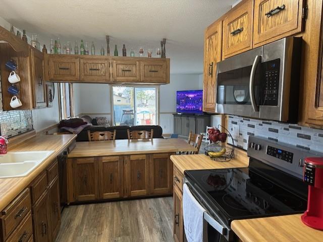kitchen featuring tasteful backsplash, light wood-style flooring, brown cabinetry, stainless steel appliances, and a sink