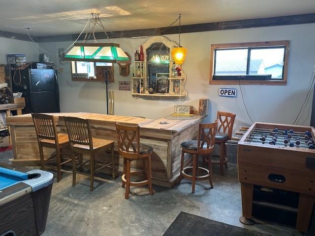 bar featuring concrete flooring, a bar, and freestanding refrigerator
