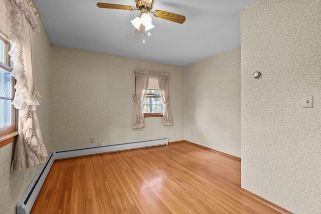 empty room featuring baseboards, baseboard heating, wood finished floors, and ceiling fan