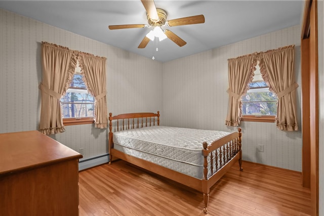 bedroom with a baseboard radiator, wallpapered walls, wood finished floors, and multiple windows