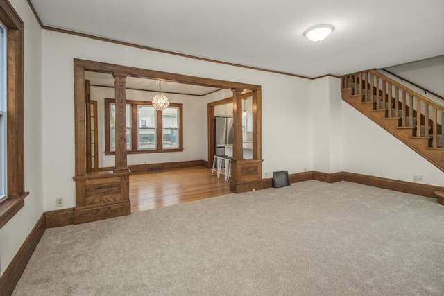 unfurnished living room featuring carpet, an inviting chandelier, ornate columns, crown molding, and baseboards