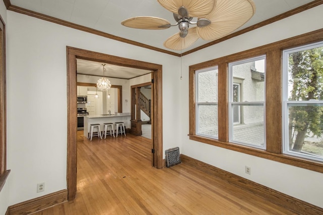spare room with stairs, ceiling fan with notable chandelier, ornamental molding, baseboards, and light wood-style floors