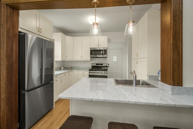 kitchen with a breakfast bar, a sink, a peninsula, light wood-style floors, and appliances with stainless steel finishes