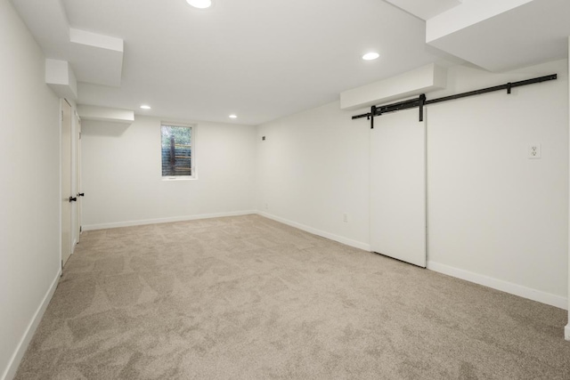 below grade area with light colored carpet, a barn door, baseboards, and recessed lighting
