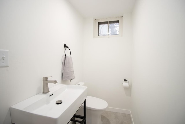 half bathroom with toilet, baseboards, and a sink