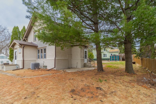 back of property featuring a storage shed, an outbuilding, fence, central AC unit, and brick siding