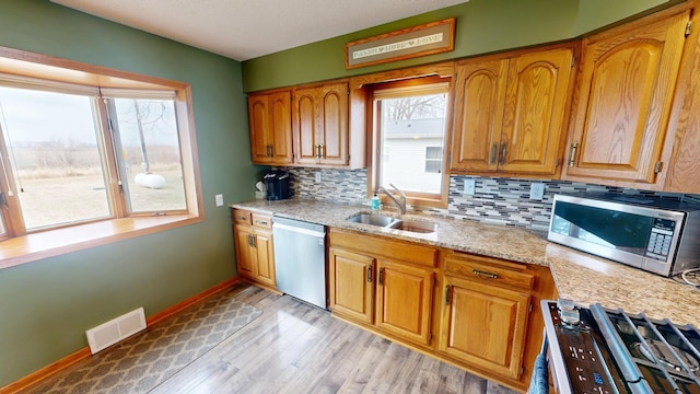 7030 147th Ave SE, Lake Lillian, MN 56253 - kitchen with stainless steel appliances, a sink, light wood-type flooring, decorative backsplash, and brown cabinets