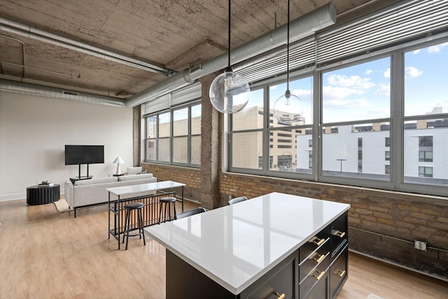kitchen with light wood-type flooring, a kitchen island, light countertops, open floor plan, and brick wall