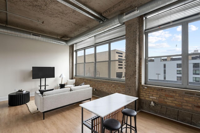 living area with visible vents, baseboards, wood finished floors, and brick wall