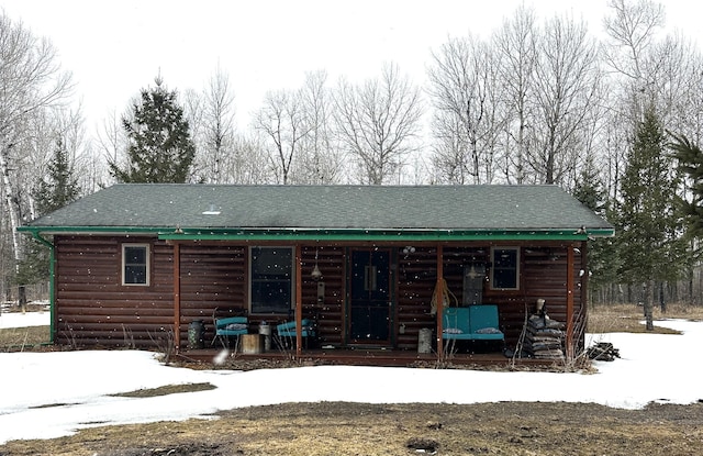 snow covered back of property with log veneer siding, a porch, and a shingled roof