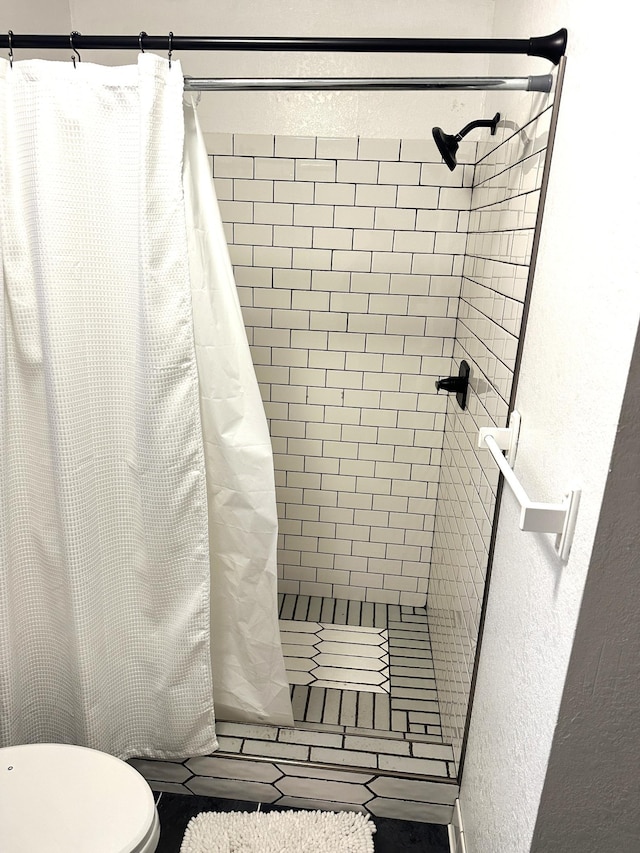 bathroom featuring a textured wall, toilet, and a stall shower