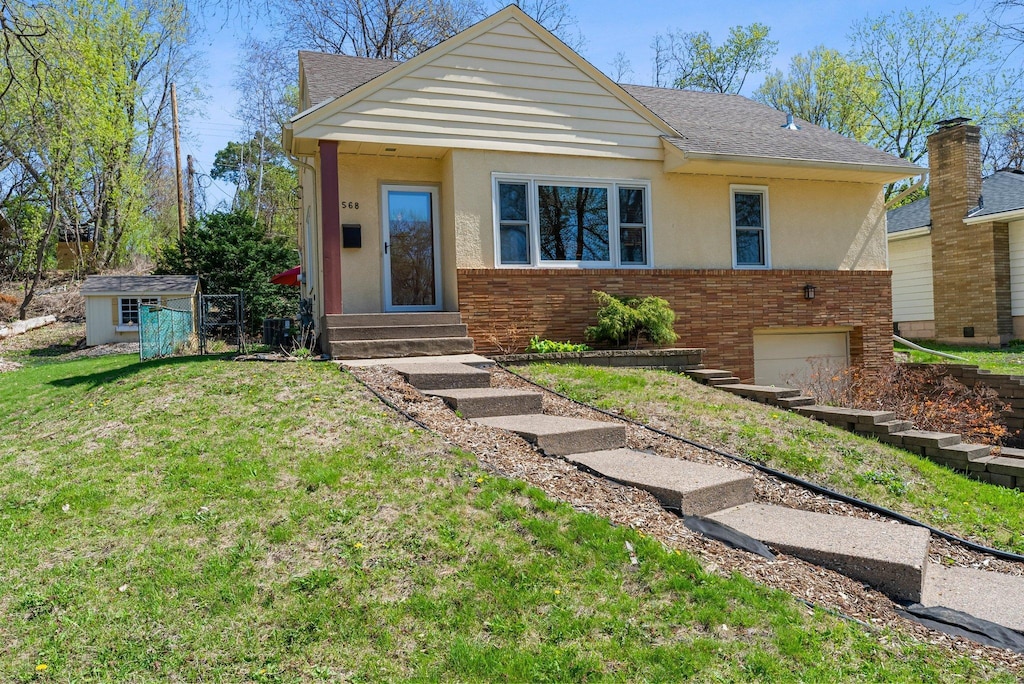 568 Frontenac Pl, Saint Paul, MN 55104 - bungalow-style home featuring stucco siding, entry steps, brick siding, a front lawn, and a shingled roof