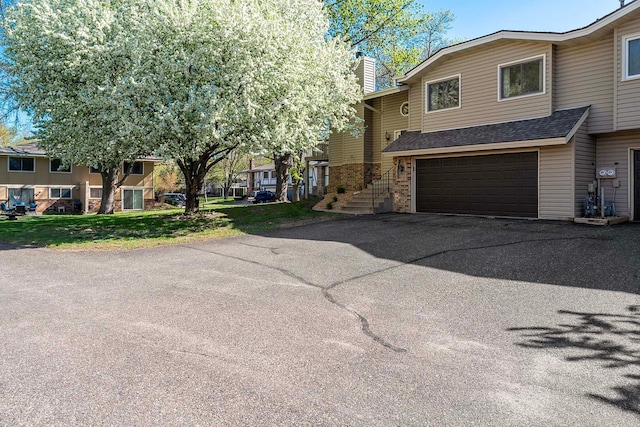 view of front of house featuring an attached garage, asphalt driveway, a shingled roof, brick siding, and a chimney