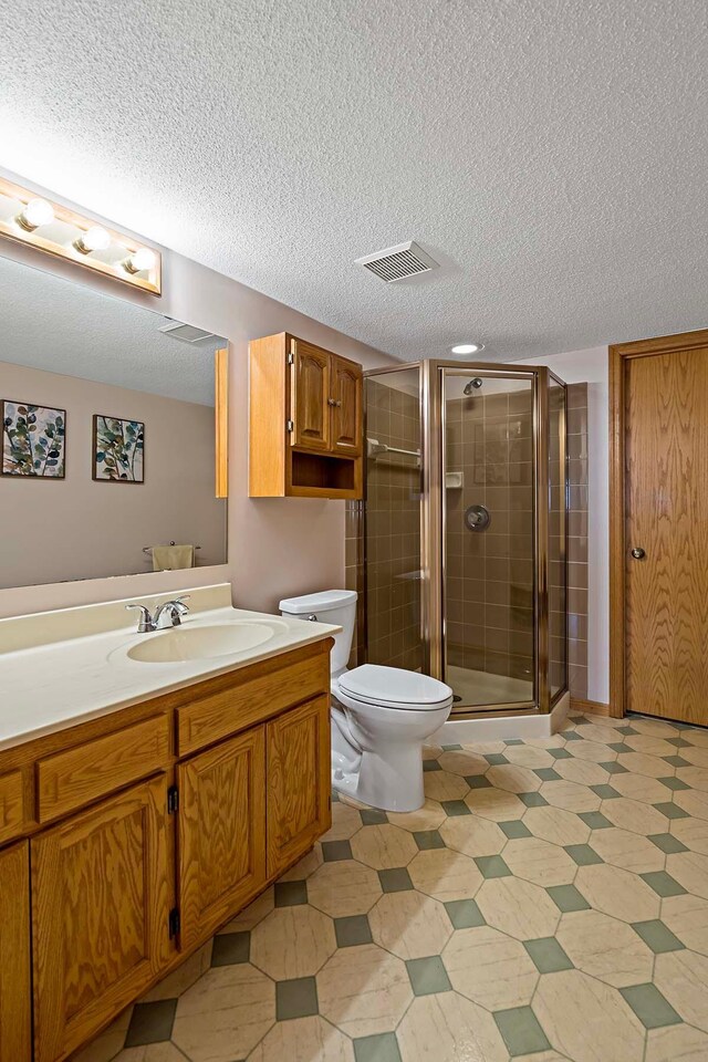 full bath featuring a textured ceiling, a shower stall, vanity, toilet, and tile patterned floors