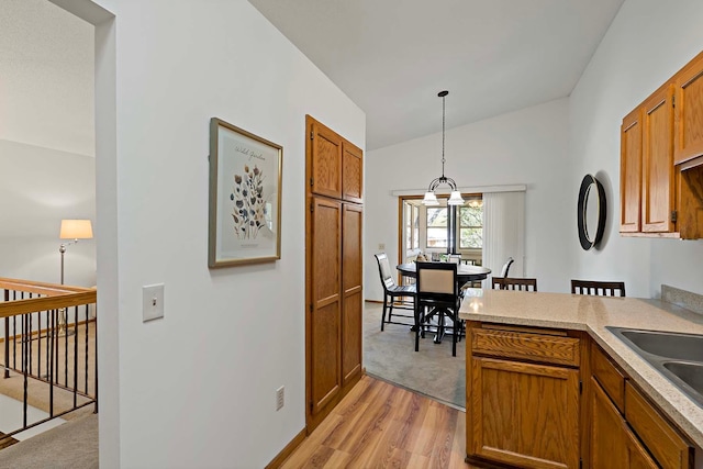 kitchen with brown cabinetry, lofted ceiling, light wood-style floors, decorative light fixtures, and light countertops