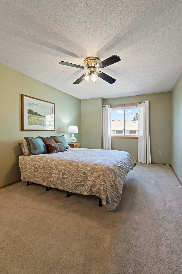 bedroom featuring light carpet, a ceiling fan, a textured ceiling, and baseboards