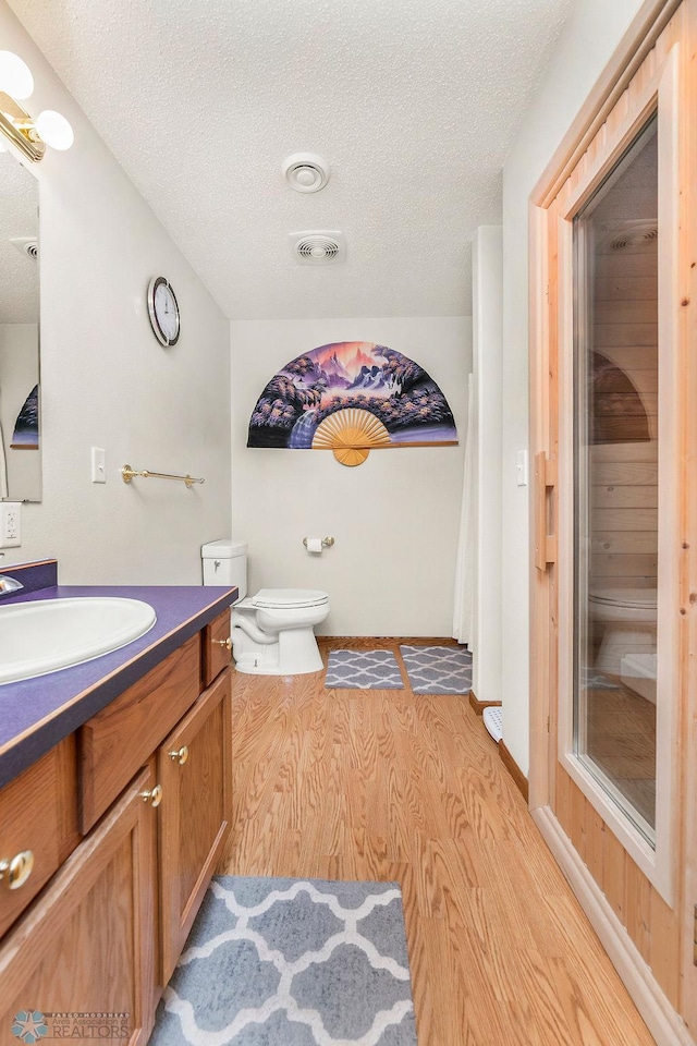 3358 70th Ave N, Moorhead, MN 56560 - bathroom featuring toilet, vanity, a textured ceiling, and wood finished floors