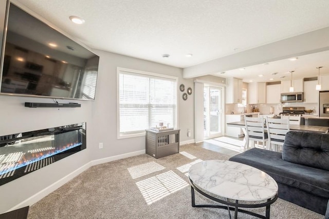 living area featuring light carpet, a glass covered fireplace, baseboards, and recessed lighting