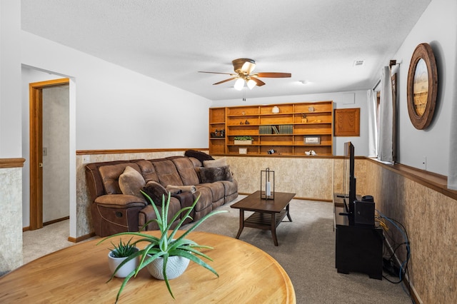 living area with a textured ceiling, ceiling fan, wainscoting, and carpet