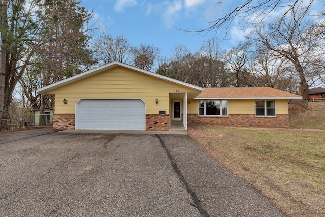 single story home featuring an attached garage, a front yard, aphalt driveway, and brick siding