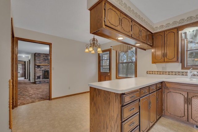 kitchen featuring light countertops, a peninsula, brown cabinetry, and a sink