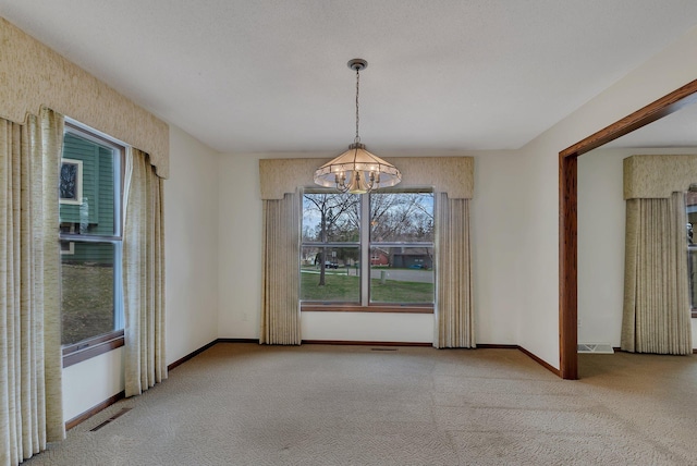 unfurnished dining area featuring baseboards, visible vents, carpet, and a chandelier