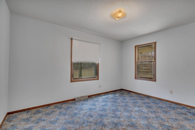 carpeted spare room with a textured ceiling, visible vents, and baseboards