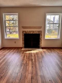 unfurnished living room with a tile fireplace, plenty of natural light, and wood finished floors