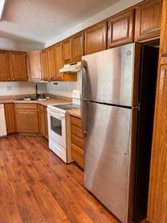 kitchen featuring freestanding refrigerator, under cabinet range hood, white electric range, wood finished floors, and light countertops
