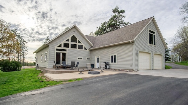 back of house with a patio, a fire pit, driveway, an attached garage, and a lawn