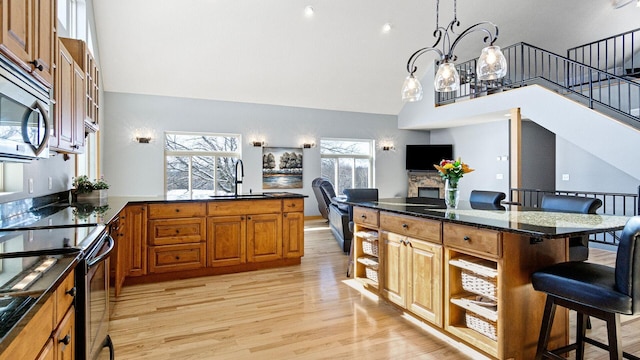 kitchen featuring light wood-style floors, brown cabinetry, stainless steel microwave, a sink, and a breakfast bar area