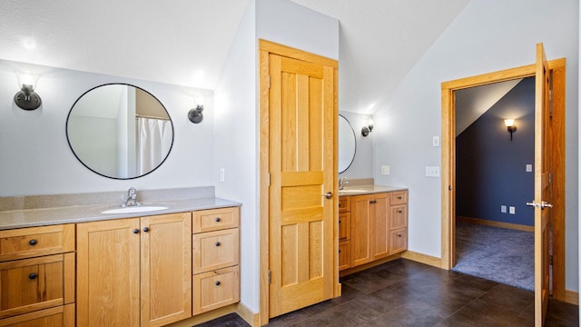 full bath featuring baseboards, two vanities, a sink, and vaulted ceiling