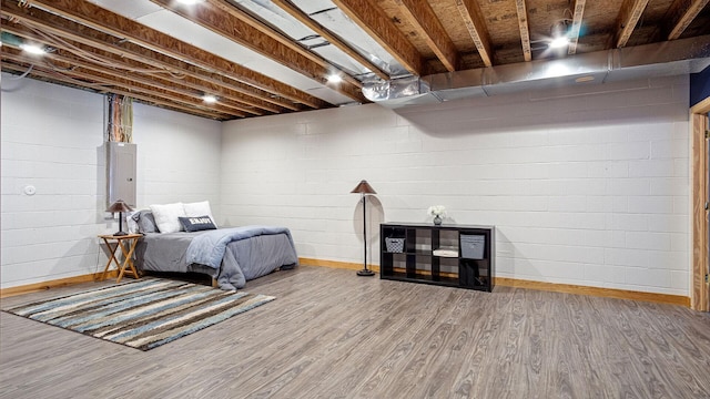 bedroom featuring baseboards, wood finished floors, electric panel, and concrete block wall