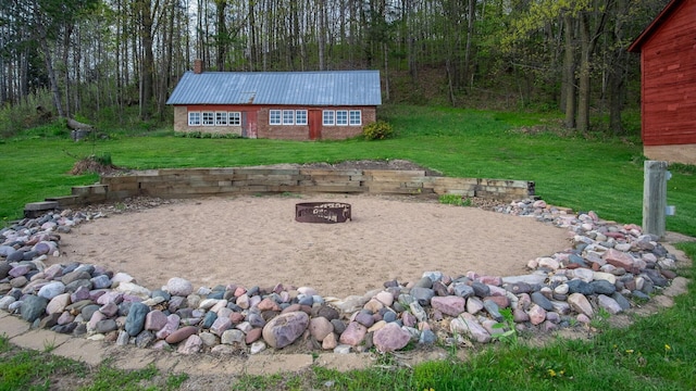 view of yard featuring a view of trees, a fire pit, and an outdoor structure