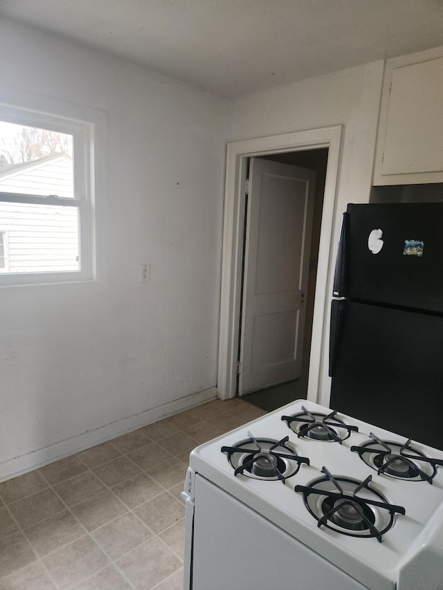 610 Grand Ave, Worthington, MN 56187 - kitchen featuring white range with gas stovetop, freestanding refrigerator, baseboards, white cabinets, and light tile patterned flooring