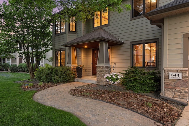 view of exterior entry with stone siding, a yard, and a shingled roof