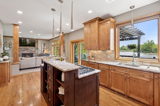 kitchen with a sink, a kitchen island, light wood finished floors, stainless steel gas cooktop, and pendant lighting